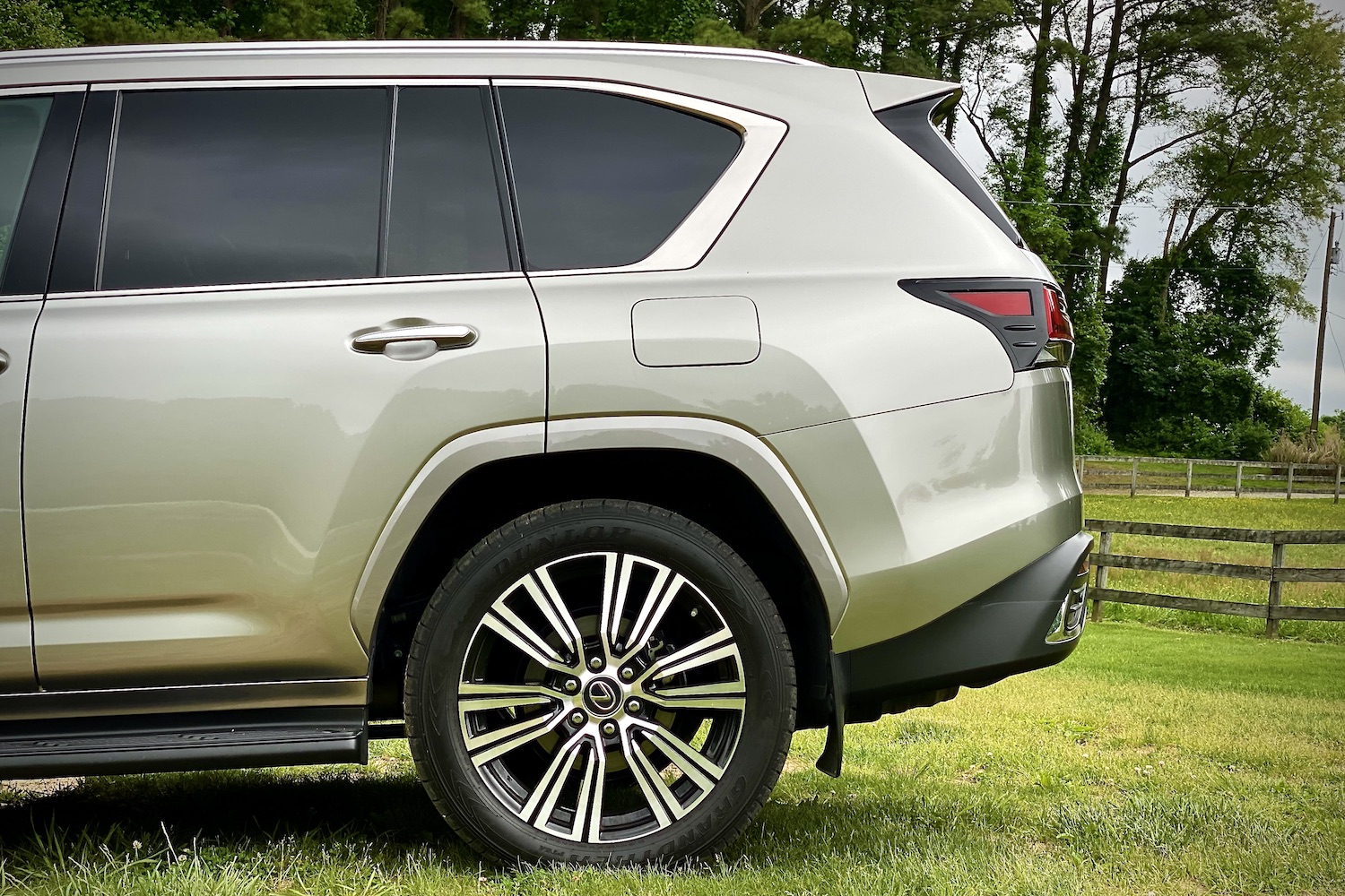 Side profile of the 2022 Lexus LX 600 rear end from the driver's side on a grassy field.