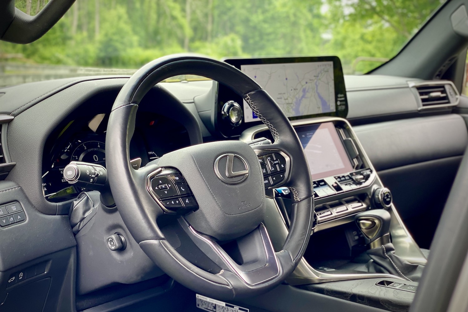 Close up of 2022 Lexus LX 600 steering wheel from outside with green trees in the back.