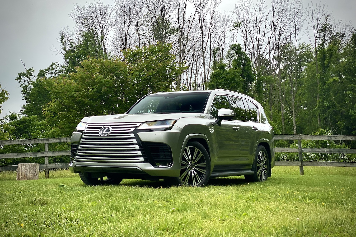 Angle of 2022 Lexus LX 600 from the driver's side with trees and a fence in the back on a grassy field.