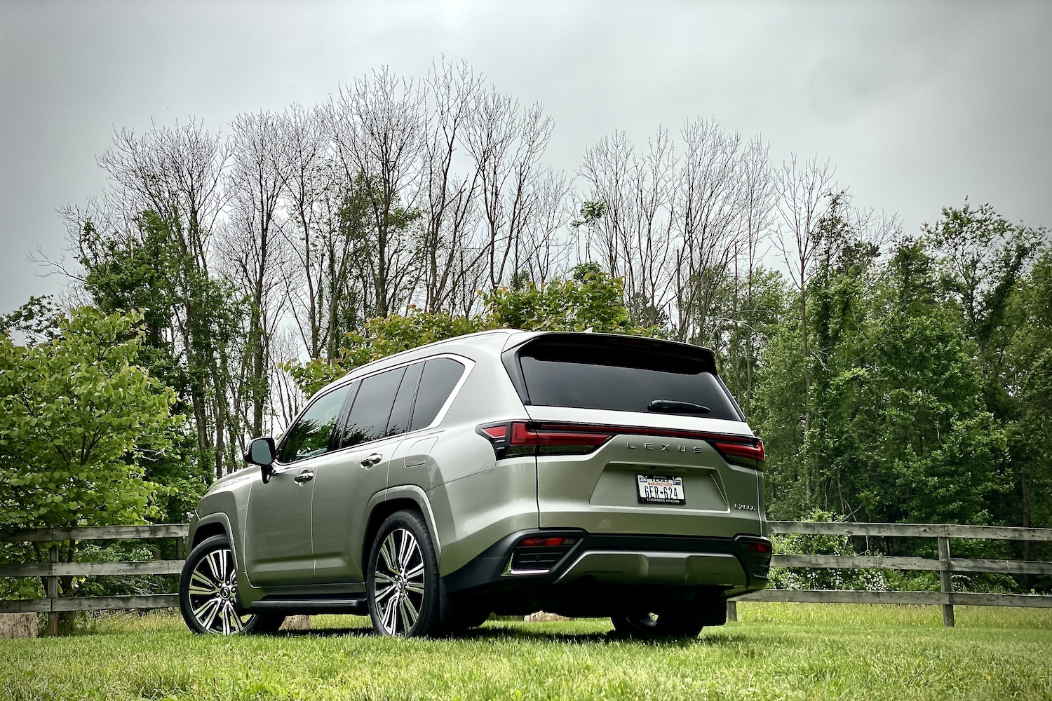 Rear end angle of 2022 Lexus LX 600 from driver's side on a grassy field with trees in the back.