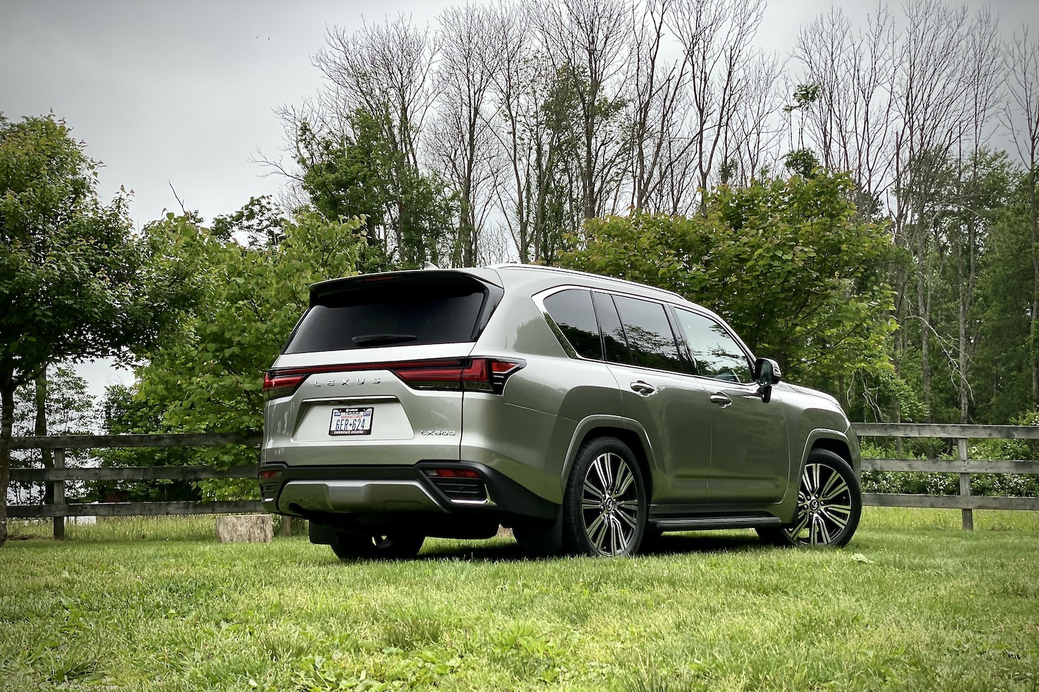 Rear end angle of 2022 Lexus LX 600 from passenger's side on a grassy field with trees in the back.