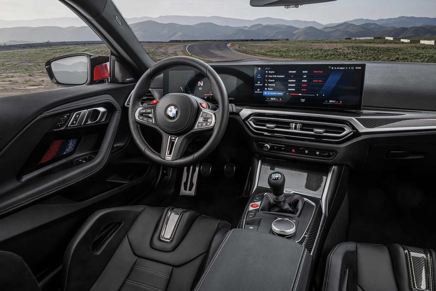 Close up of steering wheel and dashboard in 2023 BMW M2 with mountains in the back.