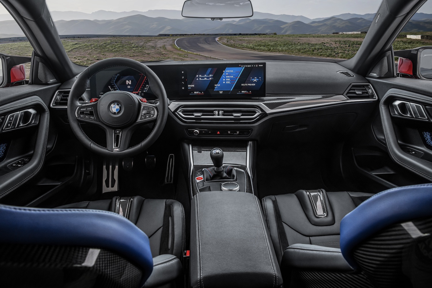 2023 BMW M2 interior from the backseats with a focus on the dashboard with mountains in the back.