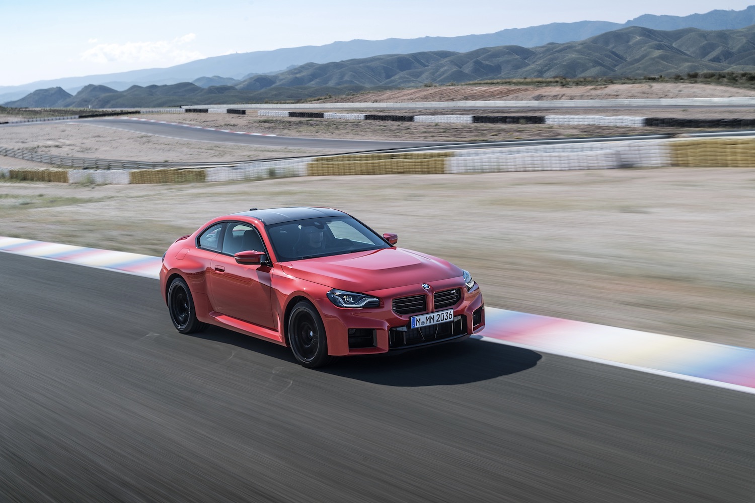 2023 BMW M2 on a race track with dirt and mountains in the back.