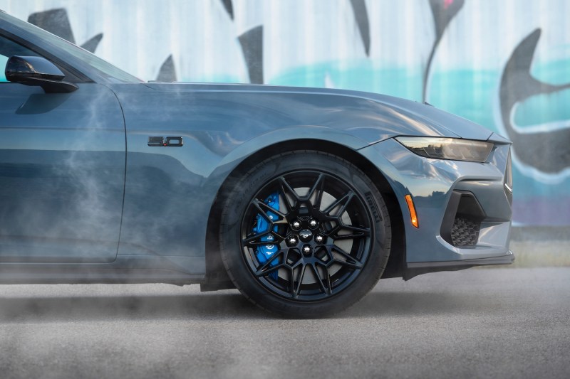 Close up of front end of 2024 Ford Mustang in front of graffiti with smoke in the front.