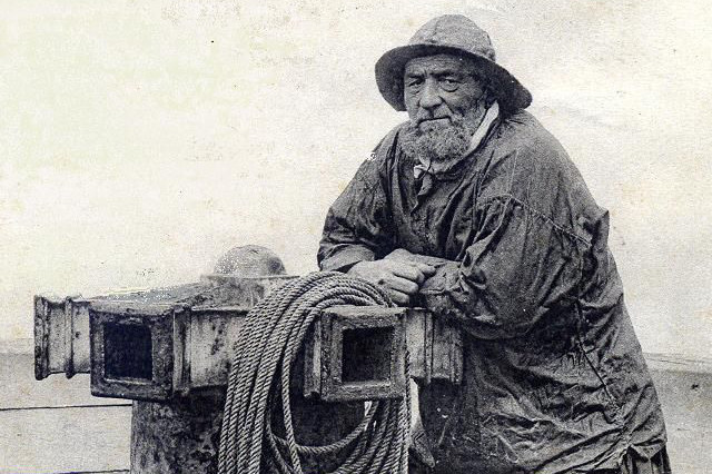 An old sailor standing on a boat in a jacket and hat