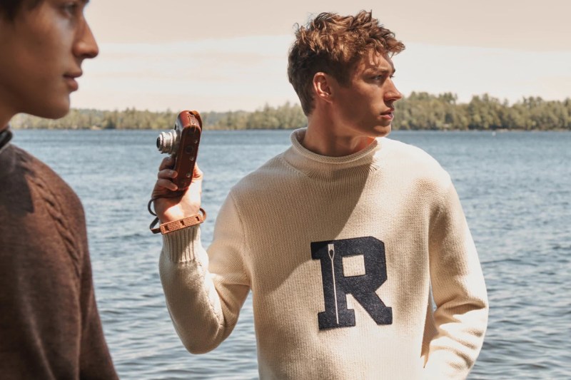 A man in a roll neck sweater standing in front of a lake.