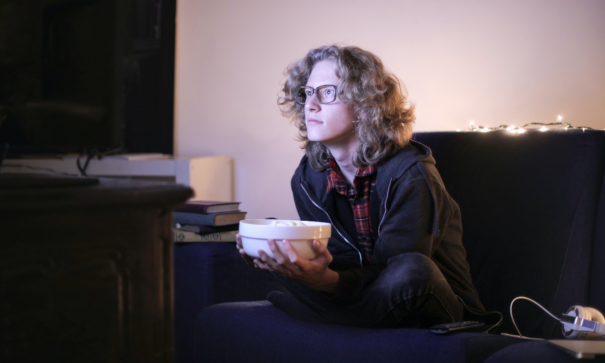 A person on their couch watching TV with popcorn