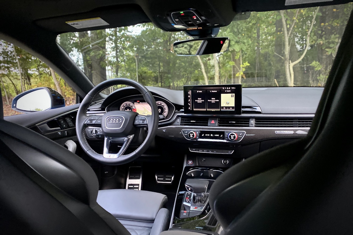 View of dashboard and steering wheel in 2023 Audi S5 Sportback with trees in the back.