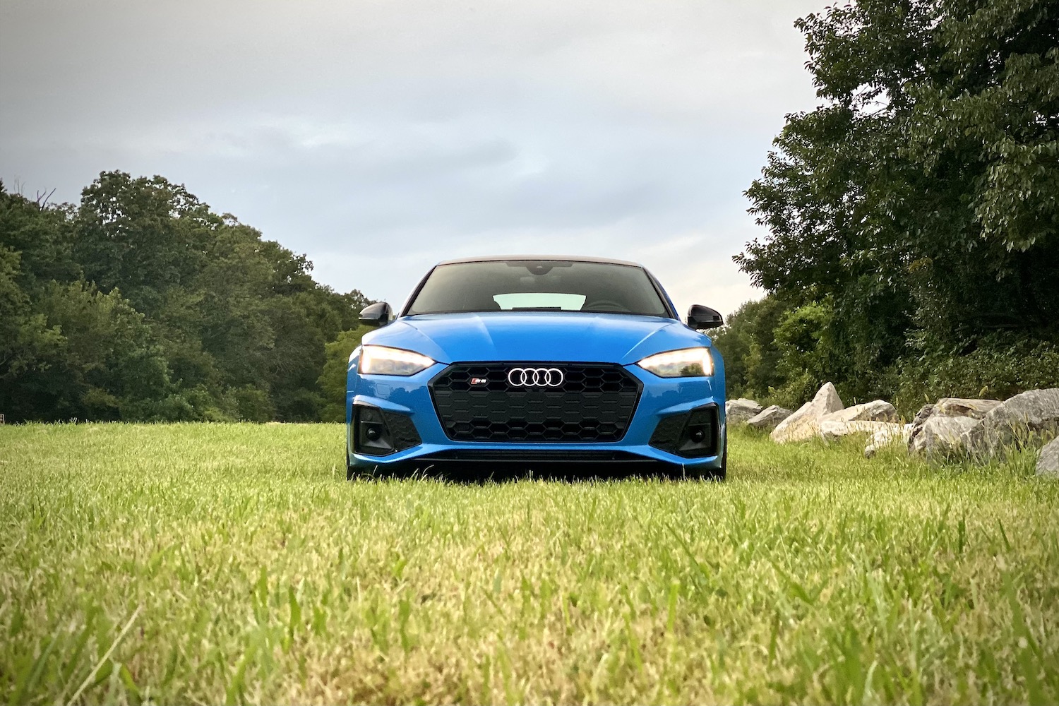 Close up of front end of 2023 Audi S5 Sportback in a grassy field during sunset.