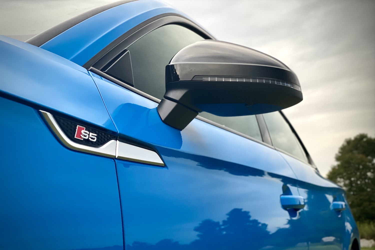 S5 badge on 2023 Audi S5 Sportback during a sunset with trees in the back.