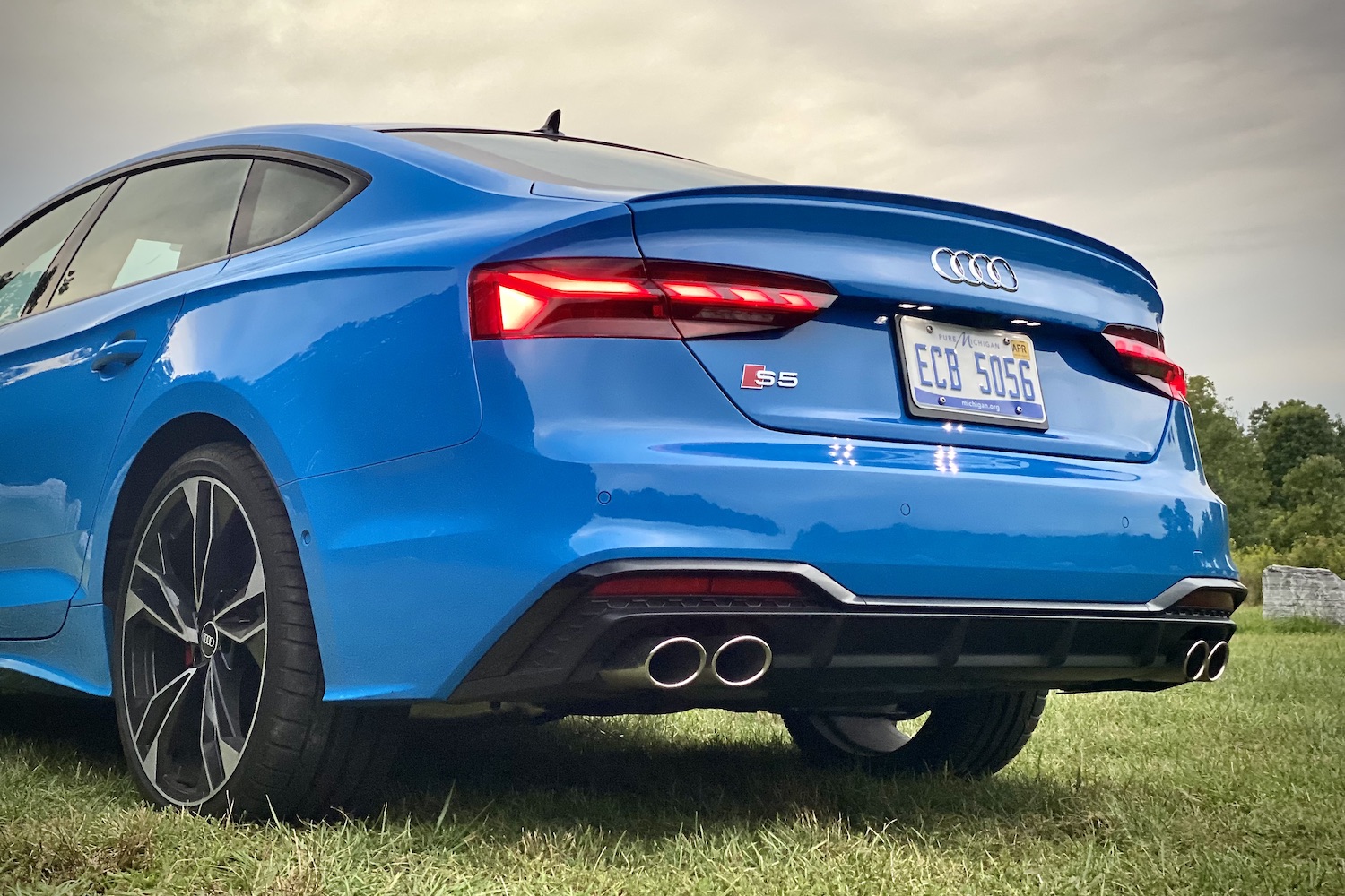 Rear end close up of 2023 Audi S5 Sportback during sunset in a grassy field.