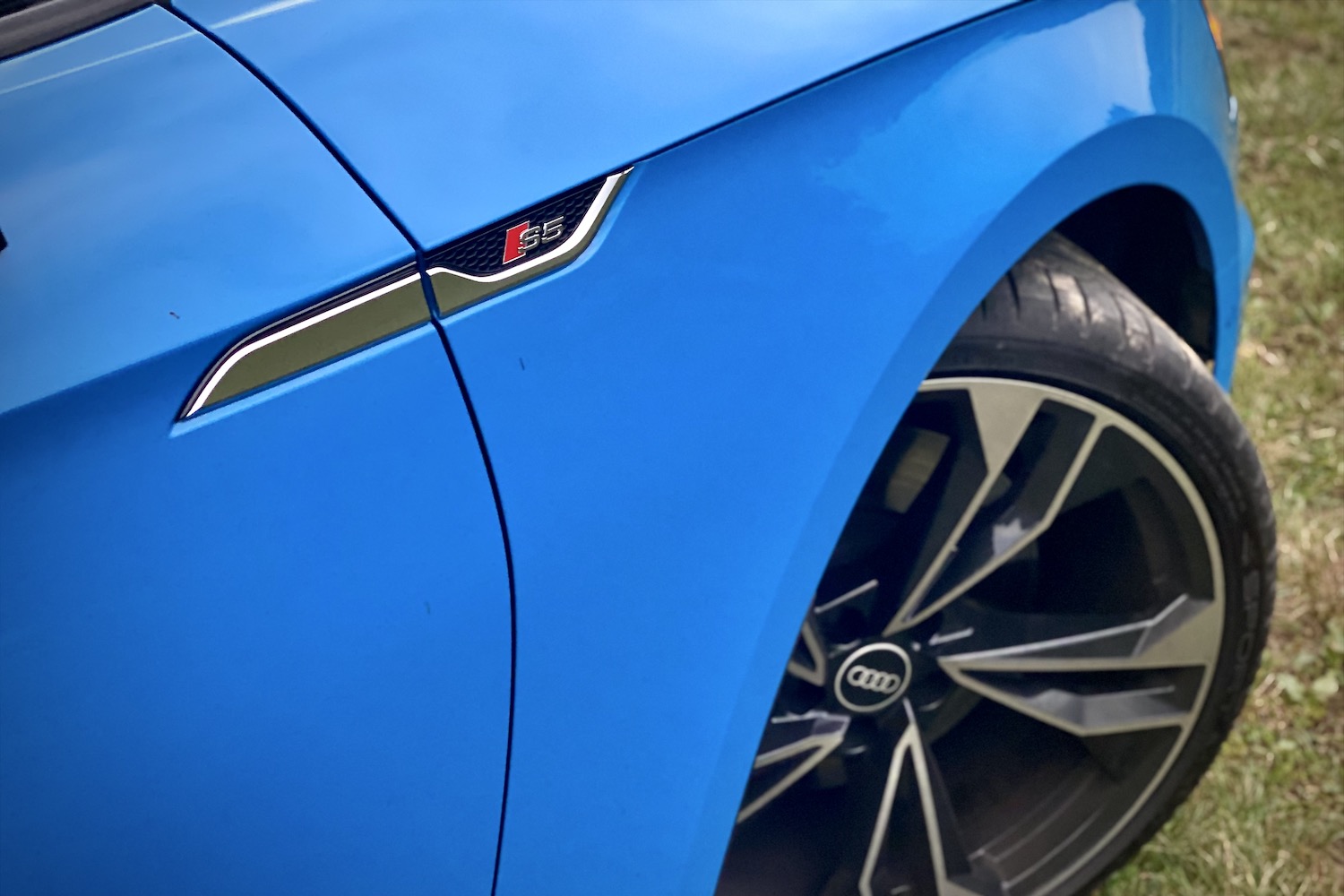Close up of front fender and wheel in the 2023 Audi S5 Sportback in a grassy field.