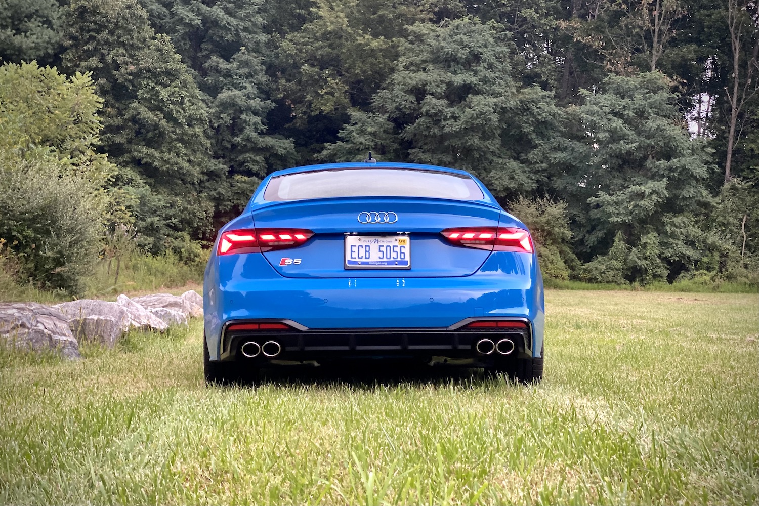 Close up of rear end of 2023 Audi S5 Sportback on a grassy field with trees in the back.