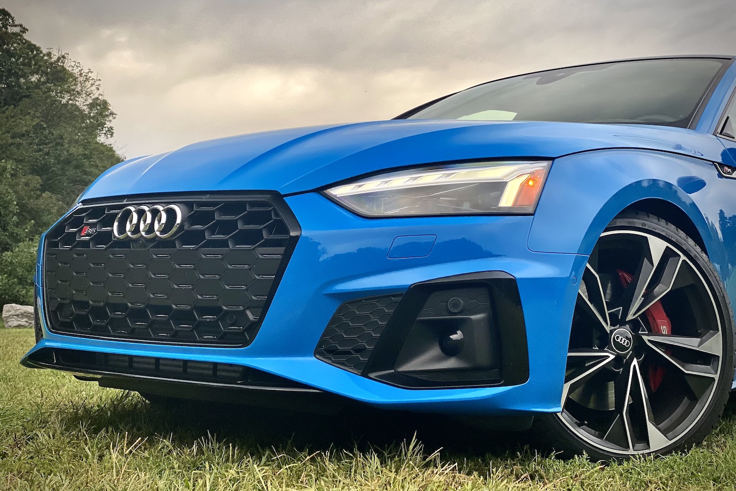 Close up of front end of 2023 Audi S5 Sportback during a sunset in a grassy field.