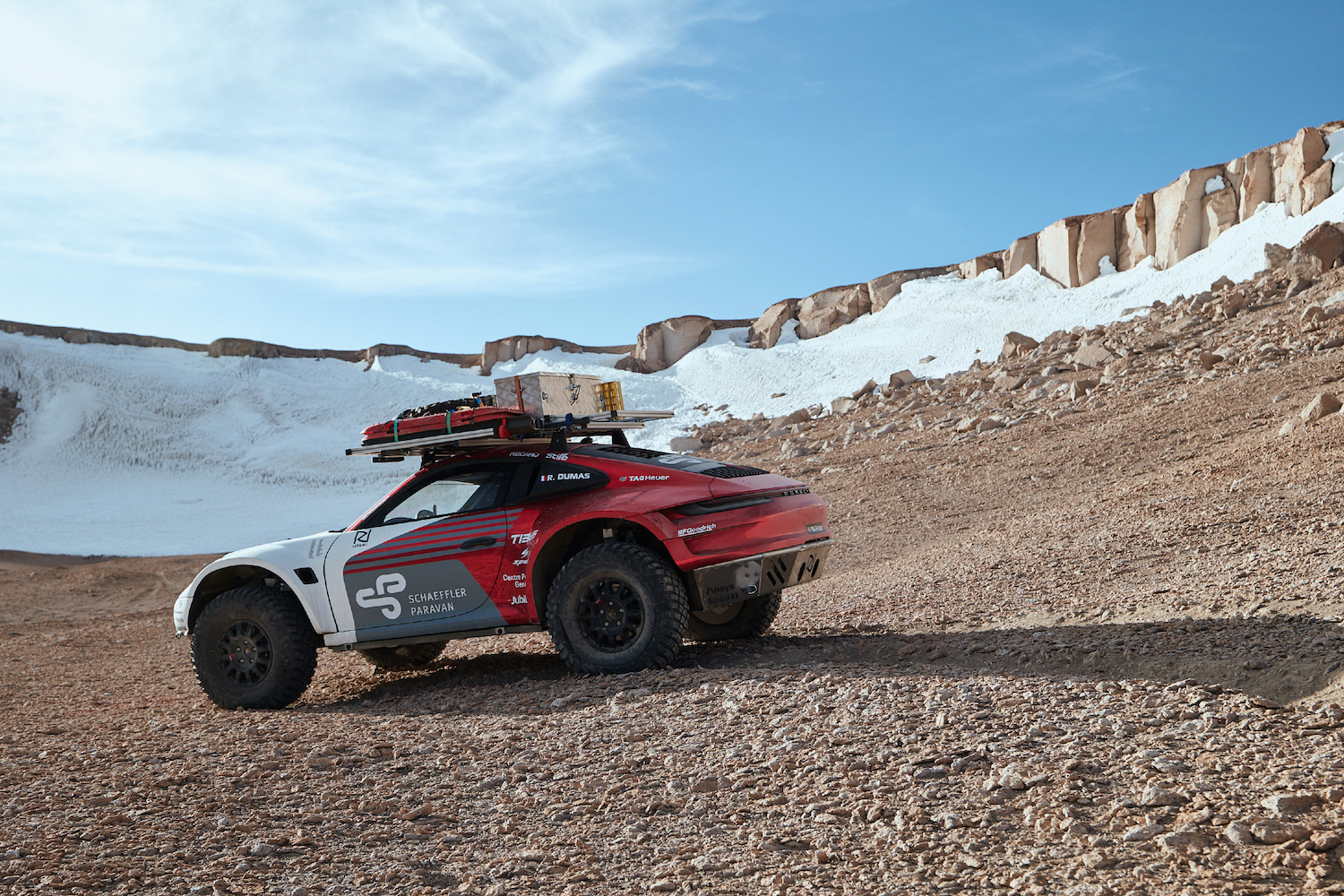 Porsche 911 Dakar Prototype going down a rocky mountain with snow in the back.