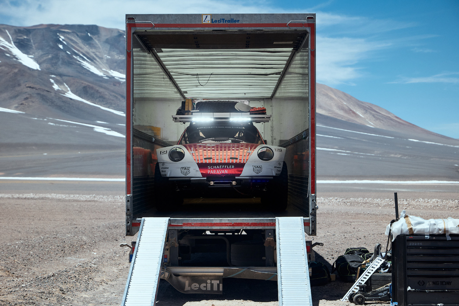 Porsche 911 Dakar Prototype close up of front end in a shipping container on rocky terrain with mountains in the back.
