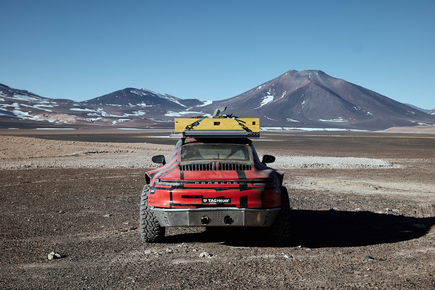 Close up of Porsche 911 Dakar Prototype rear end on rocky terrain with mountains in the back.