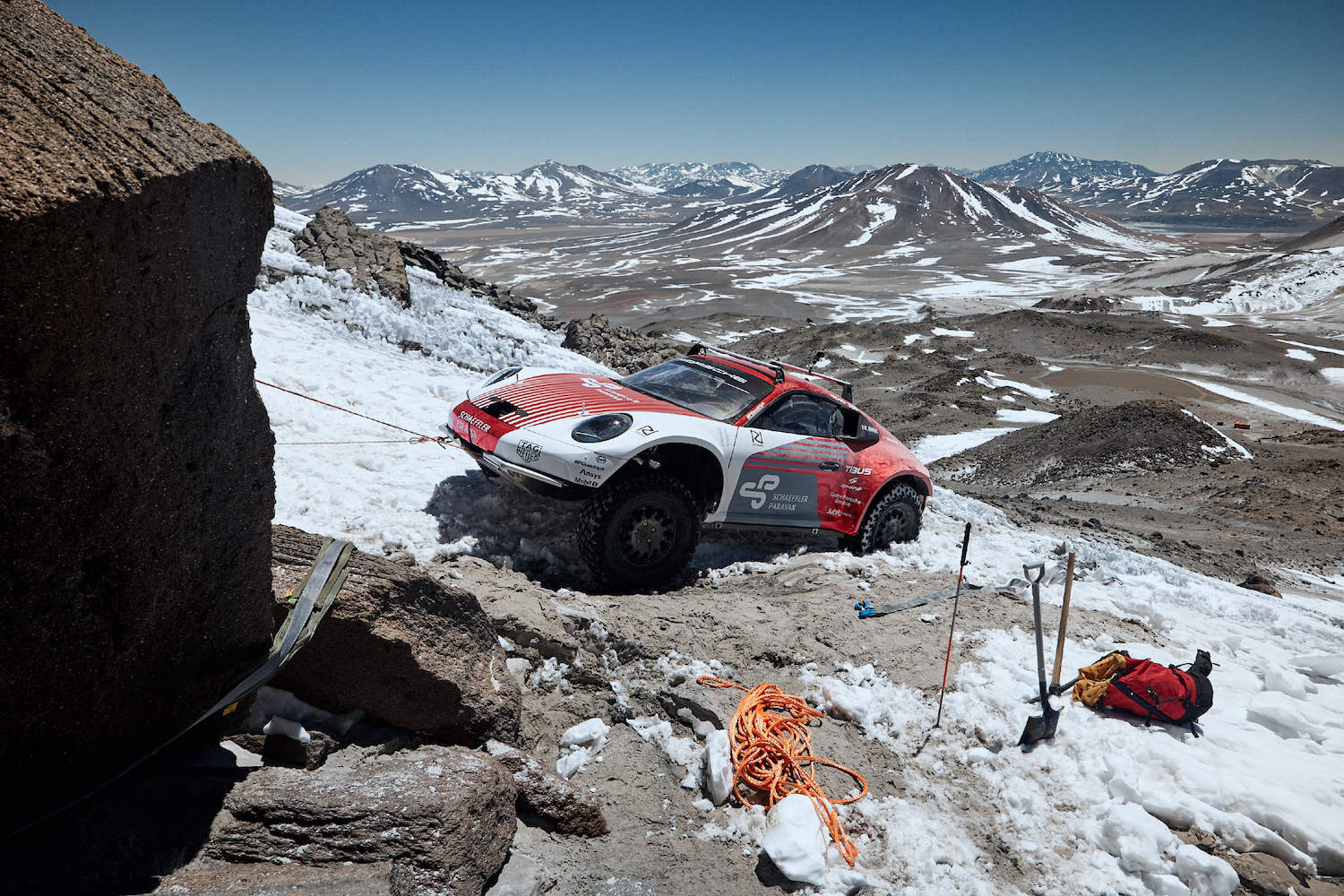 Porsche 911 Dakar Prototype climbing up a snowy volcano in Chile with mountains in the back.