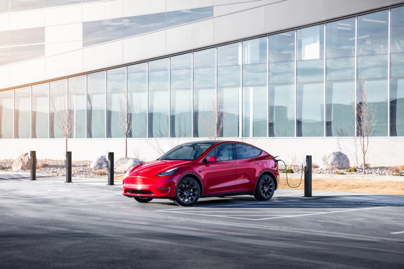 Red Tesla Model Y charging in front of a glass building with dry grass on the ground