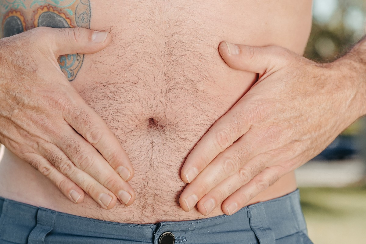 Un hombre sostiene un tatuaje en su estómago desnudo con sus manos en forma de diamante alrededor de su ombligo