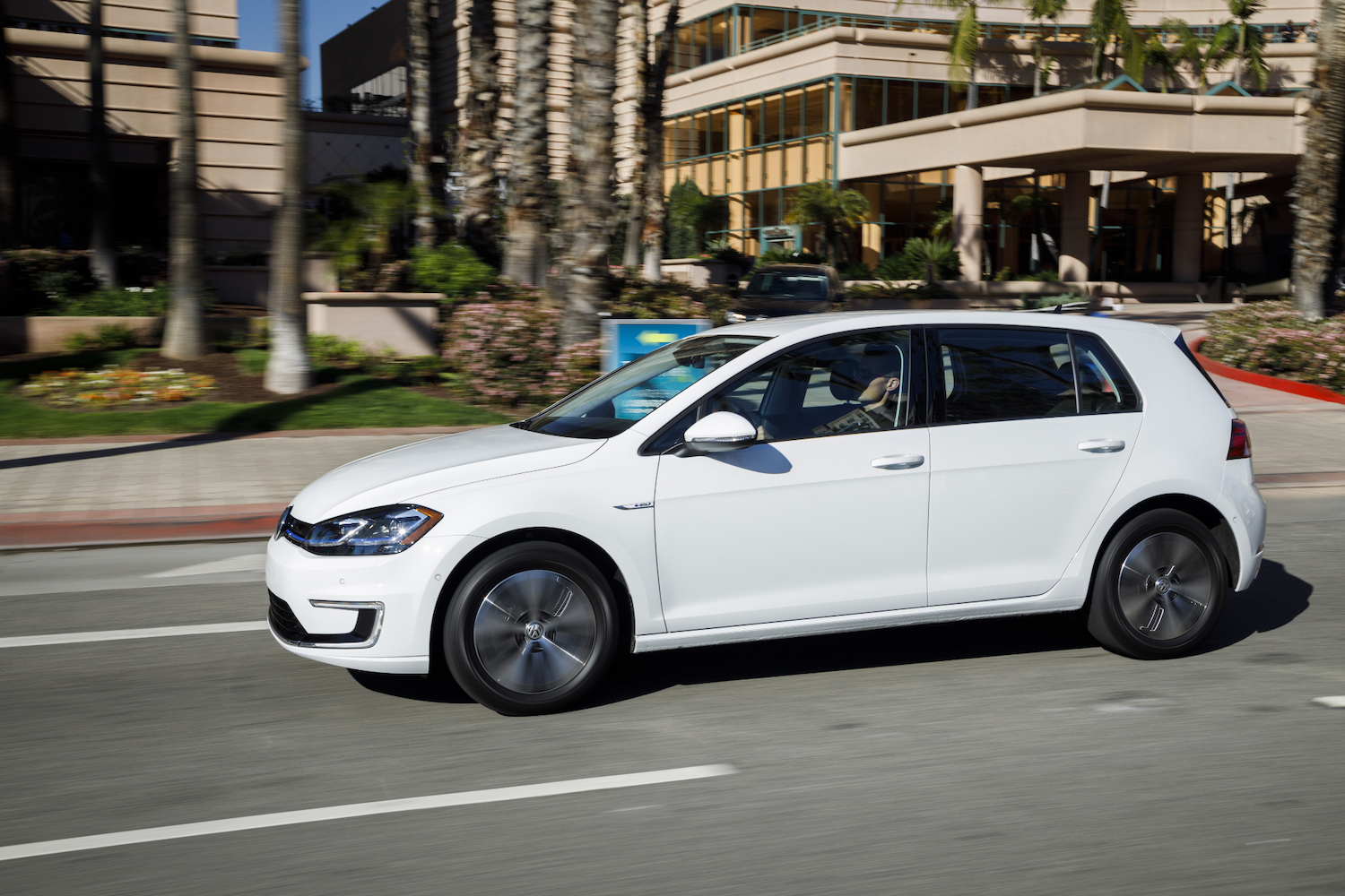 Front end angle of 2017 Volkswagen e-Golf driving down the road in front of buildings.