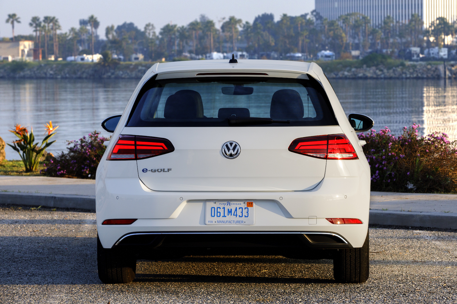 Rear end close up of 2017 Volkswagen e-Golf parked in front of a river with tall buildings in the back.