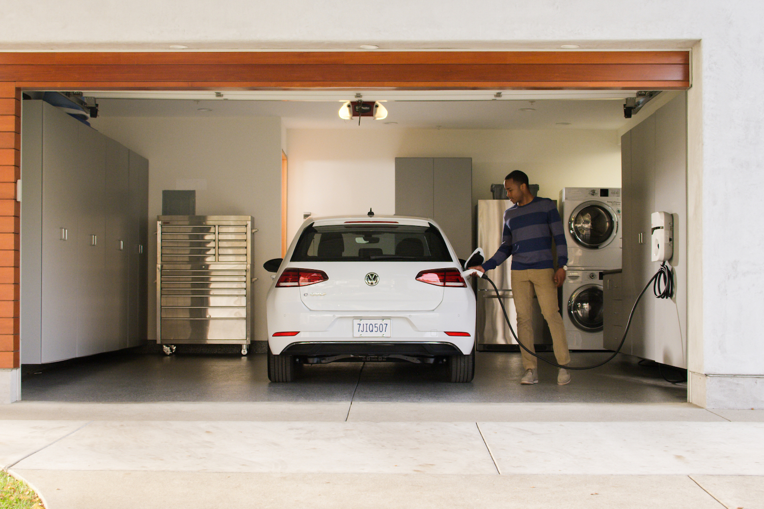 Man plugging a charging cable into a 2017 Volkswagen e-Golf in a garage.