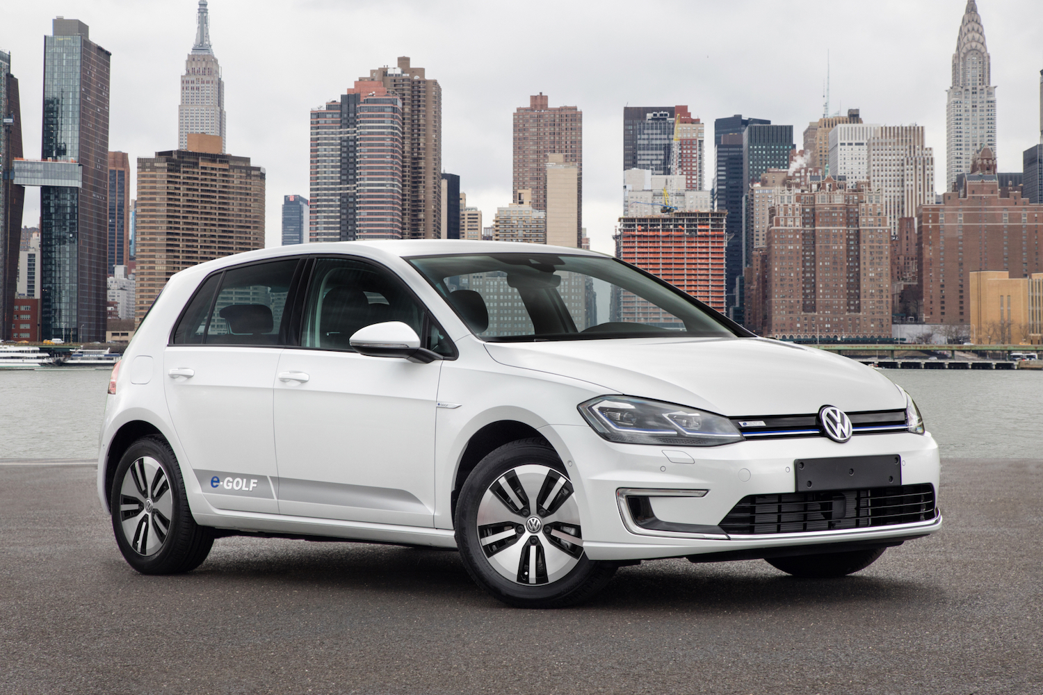 2017 Volkswagen e-Golf front end passenger's side angle parked in front of a city with tall buildings.