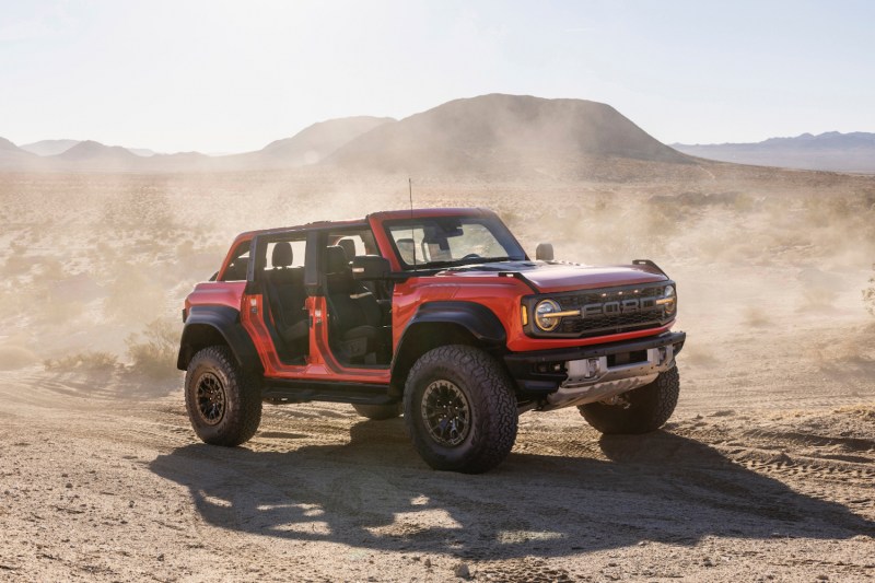 2022 Ford Bronco Raptor off-roading through sand dunes with the doors and roof off the SUV with a dust cloud in the back.