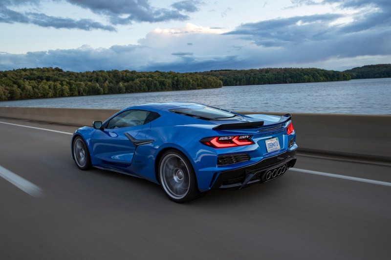 2023 Chevrolet Corvette Z06 rear end angle from driver's side driving on the road in front of a body of water with clouds in the back.