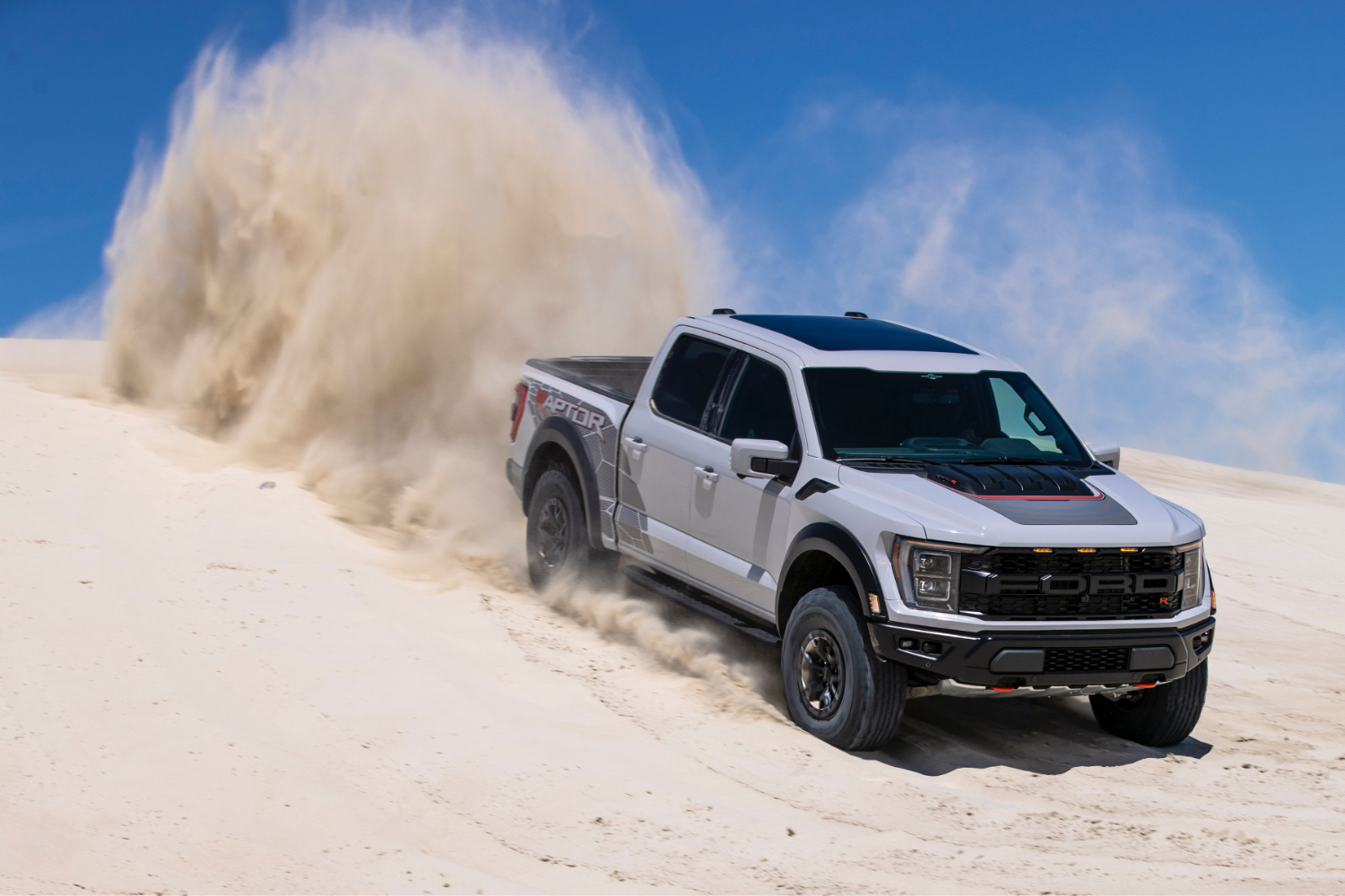 2023 F-150 RAPTOR R Front vége az utas oldalától, a Vezetéssel egy homokdűnel, kék ég hátulján