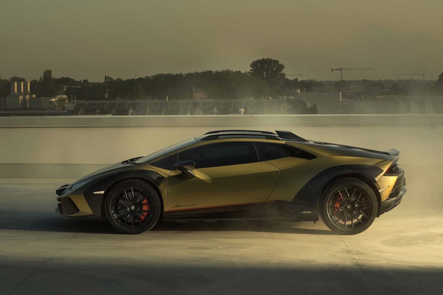 Side profile of 2023 Lamborghini Huracan in front of a city with smoke in the back during sunset.