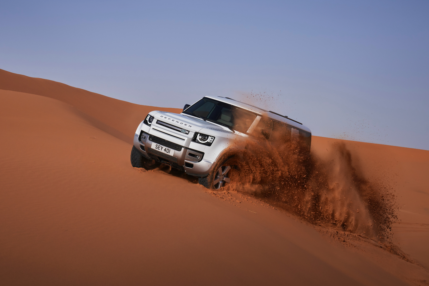 2023 Land Rover Defender 130 Elülső vége a sivatagban lévő homokdűne áthaladva, hátul kék égbolt