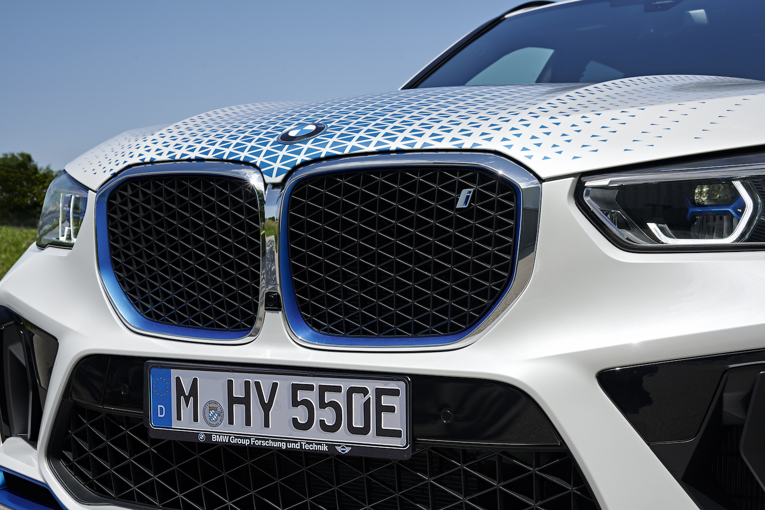 BMW iX5 Hydrogen close up of front end black grilles and badges with blue skies in the back.