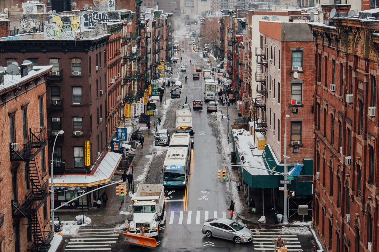 East coast city in winter with snow on the ground and on top of apartment buildings with cars on the road.