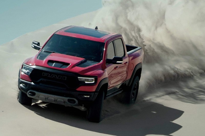 Front end of 2022 Ram 1500 TRX power sliding on a sand dune in the desert with blue skies in the back.