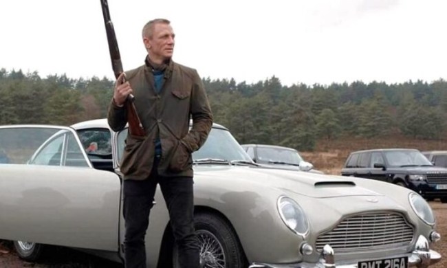 James Bond holding a shotgun and standing next to an Aston Martin