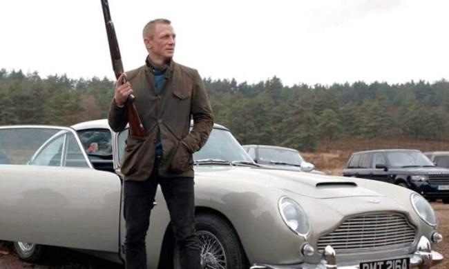 James Bond holding a shotgun and standing next to an Aston Martin