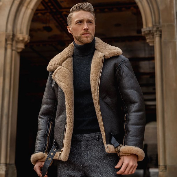 Man in a black turtle neck, black and tan shearling jacket, and gray knit pants