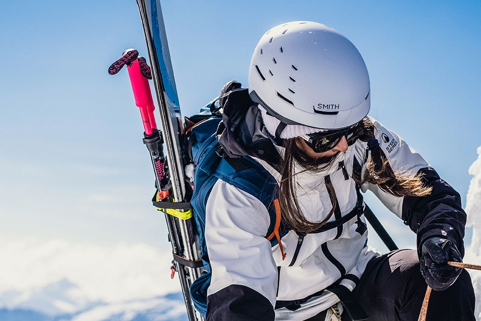Woman with skis climbing mountain wearing Smith Summit Helmet.