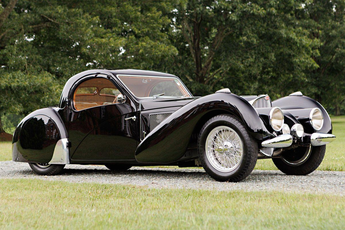 1937 BUGATTI TYPE 57SC ATALANTE side profile from passenger side parked in a field with green trees in the back.