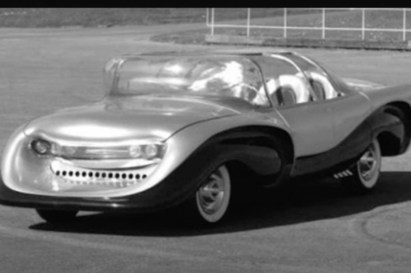 Ángulo frontal del auto de seguridad Aurora de 1957 desde el lado del conductor estacionado en un estacionamiento de tierra.