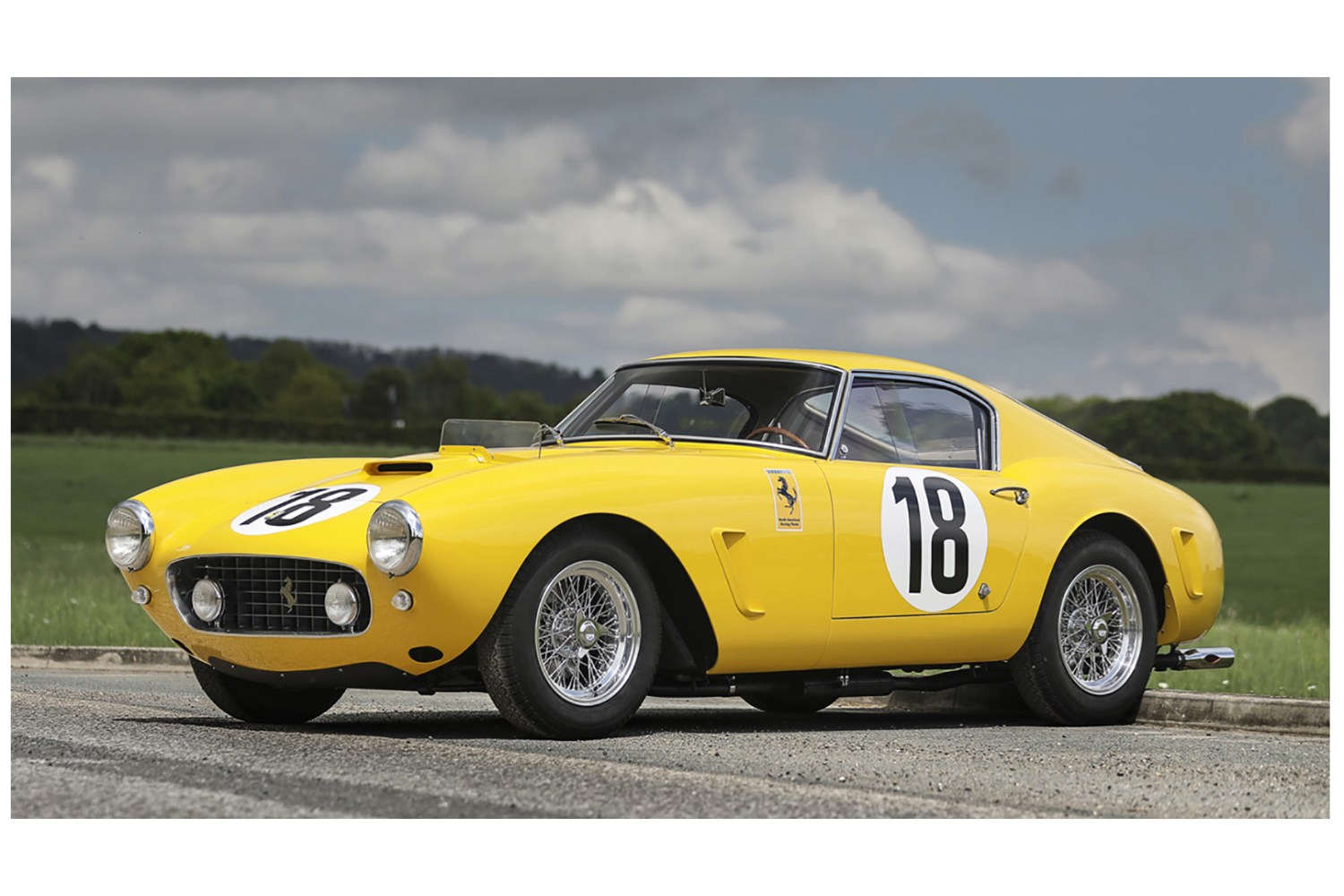 1960 Ferrari 250 GT SWB Berlinetta Competizione front end angle from driver's side parked in font of green hills and clouds.