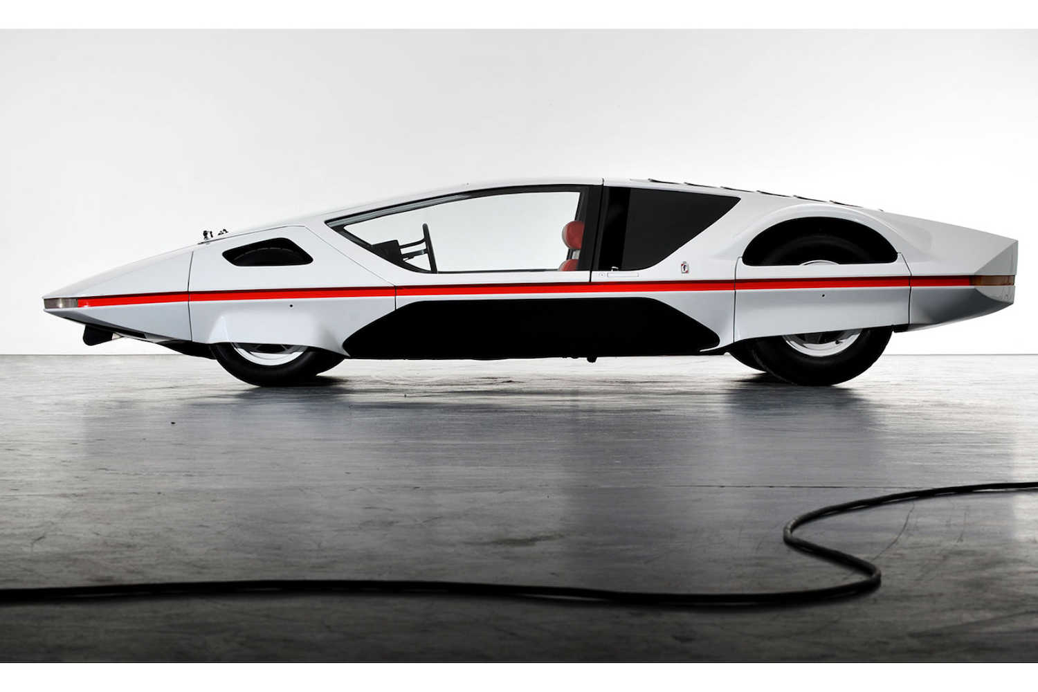Side profile of 1970 Ferrari Modulo parked in front of a white wall on top of a gray floor.
