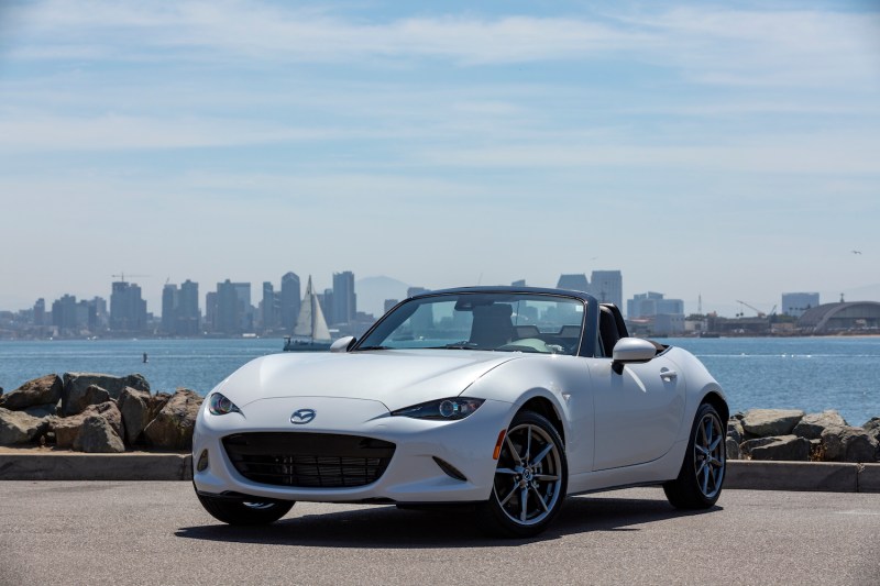 2019 Mazda MX-5 Miata front end angle from driver's side with top down parked in front of a city skyline.