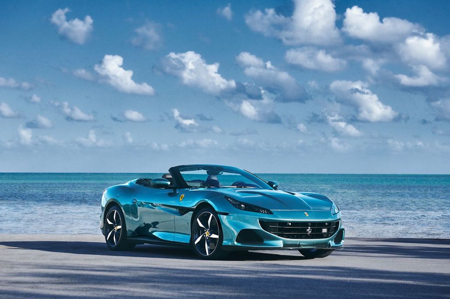 2021 Ferrari Portofino M front end angle parked in front of a beach with blue skies in the back.