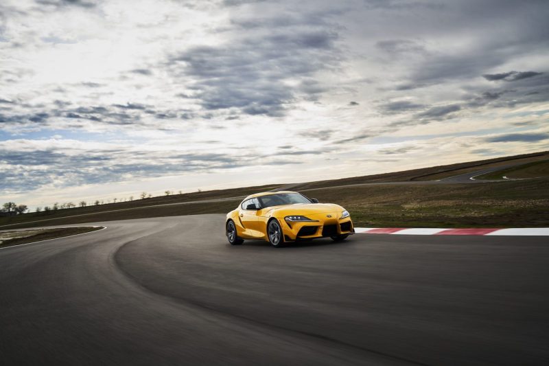 2022 Toyota GR Supra 2.0 front end driving on a race track with clouds in the back ground.
