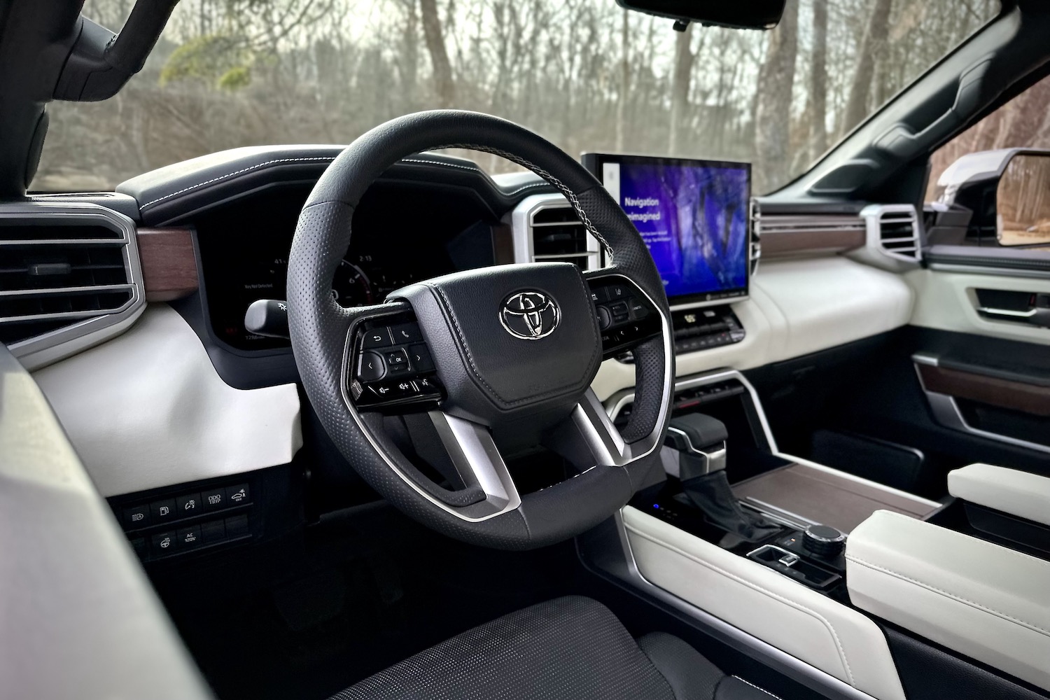 Close up of steering wheel in the 2022 Toyota Tundra Hybrid Capstone from outside the truck with trees in the background.