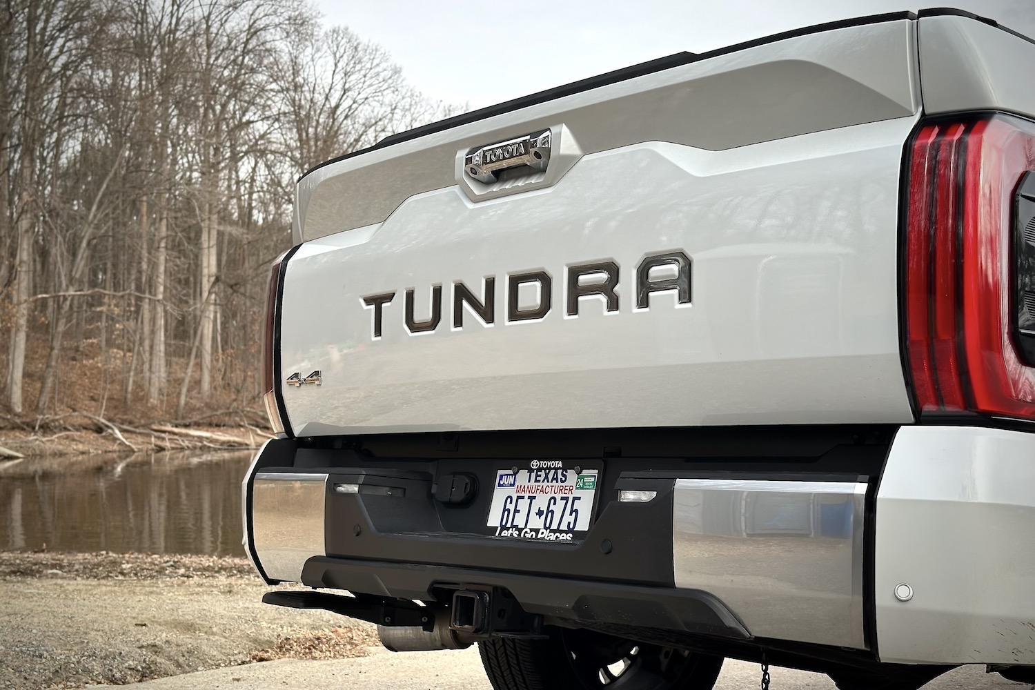 Close up of Tundra badged on the back of the 2022 Toyota Tundra Hybrid Capstone with trees in the background.